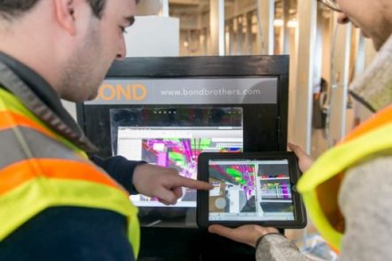 Two BOND Staff Members in front of a BIM Box with a tablet looking at the Revit CADD model of the installation at a job site.