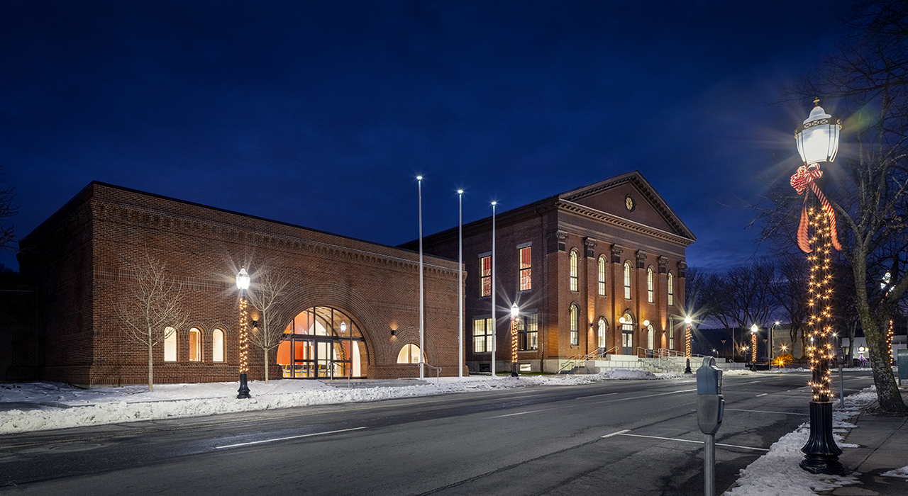 Exterior of Fitchburg City Hall at night in the winter. Building complex is shot at an angle and shows historic building and former bank at left renovated into Legislative Chambers.