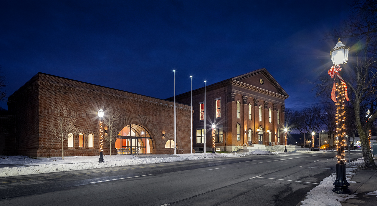 Exterior of Fitchburg City Hall at night in the winter. Building complex is shot at an angle and shows historic building and former bank at left renovated into Legislative Chambers.