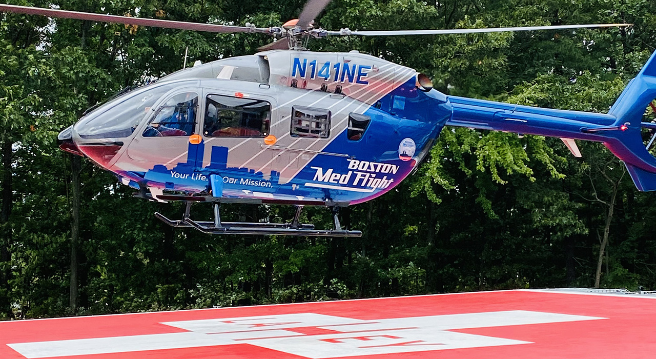 Medflight helicopter landing on a helideck with a bright red base and a square medical logo.