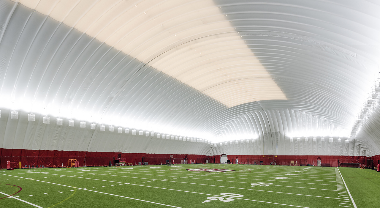 Interior of a Seasonal Air Supported Athletic Facility. Logo of UMass Amherst in foreground. White inflatable structure over field.