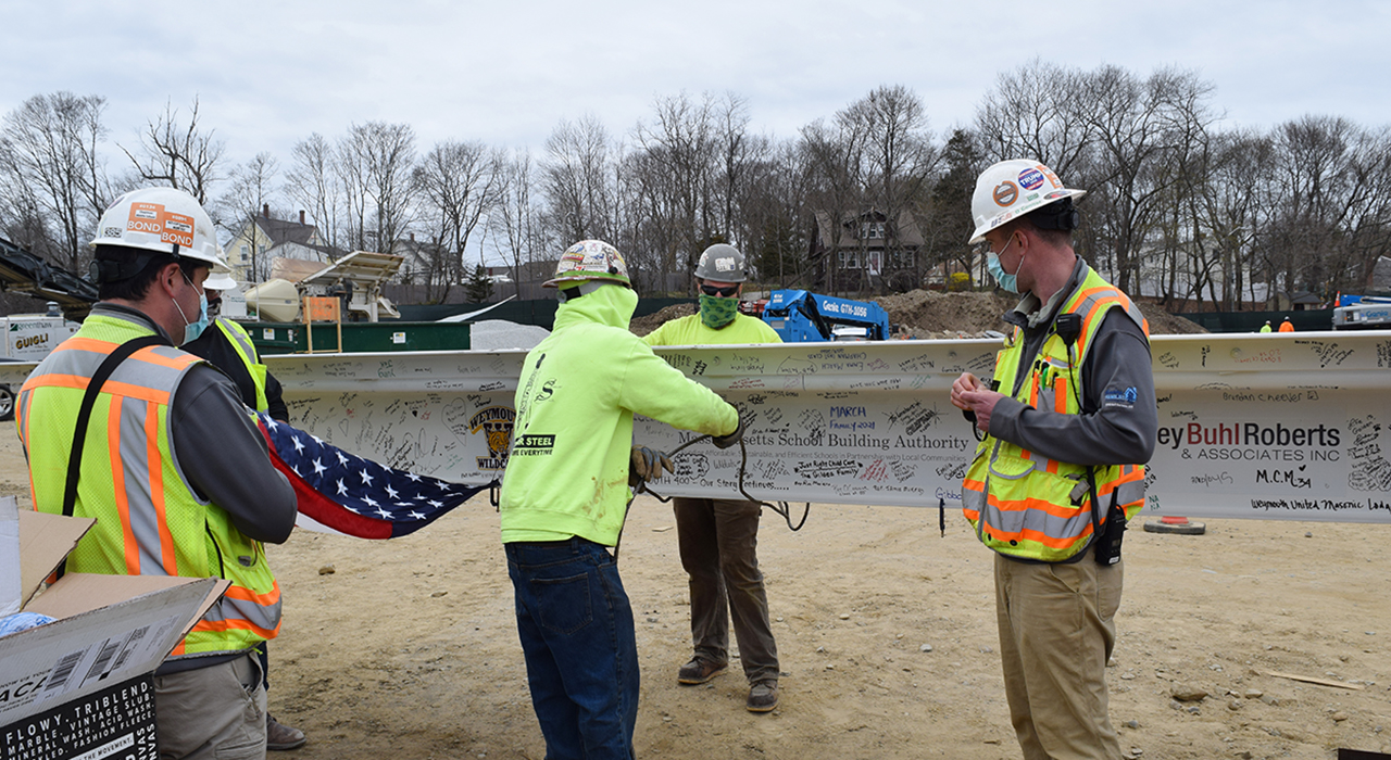 Weymouth Maria Chapman West Middle School Topping Off. Four construction workers with steal beam signed by townspeople and with logos of the firms involved.